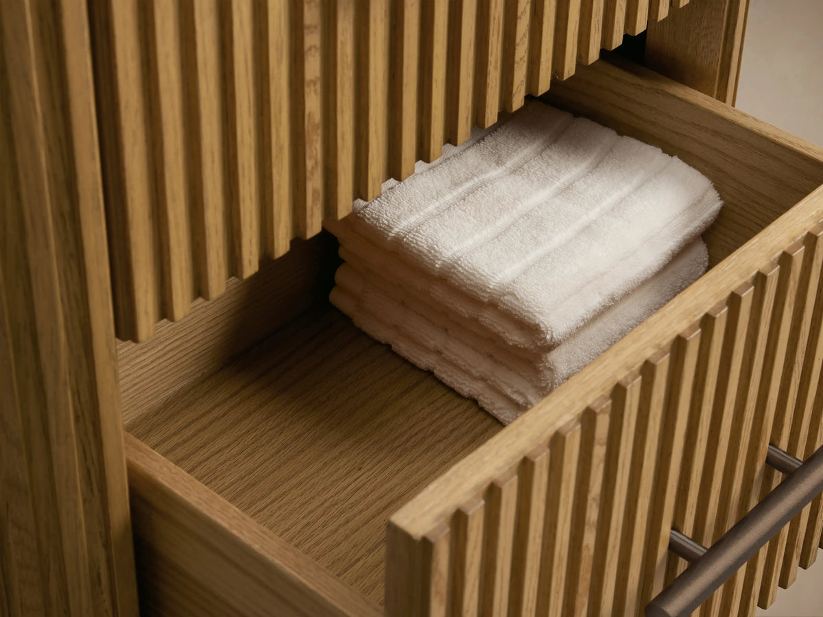 Close-up of Finnley Short Bath Cabinet: dark gray honed stone top, vertically fluted natural oak wood, antique bronze handle.