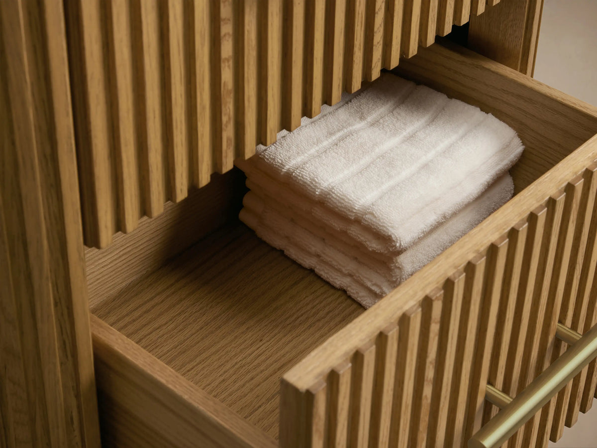 Finnley Short Etagere with vertical oak slats, three drawers, antique brass handles, and dark stone top on tiled floor.