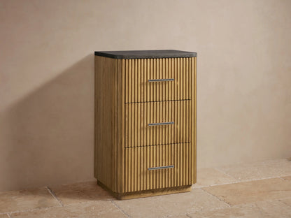 Finnley Short Etagere featuring vertical oak slats, black stone top, three drawers with polished nickel handles, in a beige alcove.
