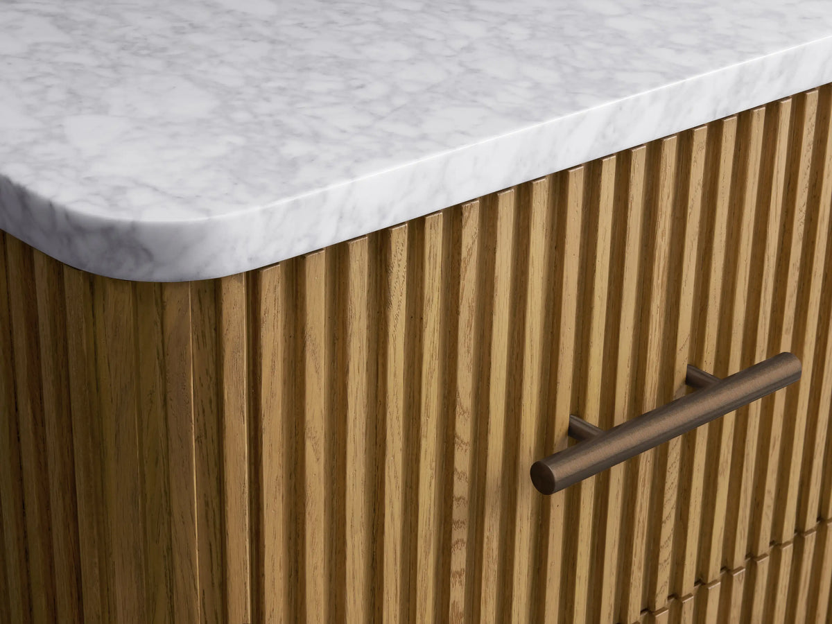 Finnley Short Bath Cabinet, a light fluted oak wood cabinet with a white marble top and three drawers with dark bronze handles.