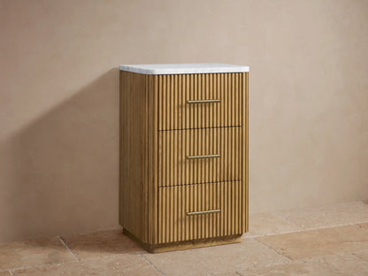 Finnley Short Etagere with vertical slat oak wood design, three drawers, brass handles, and a sealed stone top, against a neutral background.