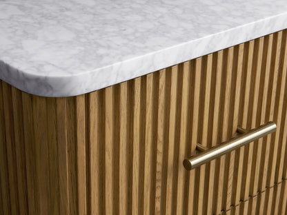 Finnley Short Etagere with ribbed oak wood finish, white marble top, and three drawers with metal handles, against beige wall.