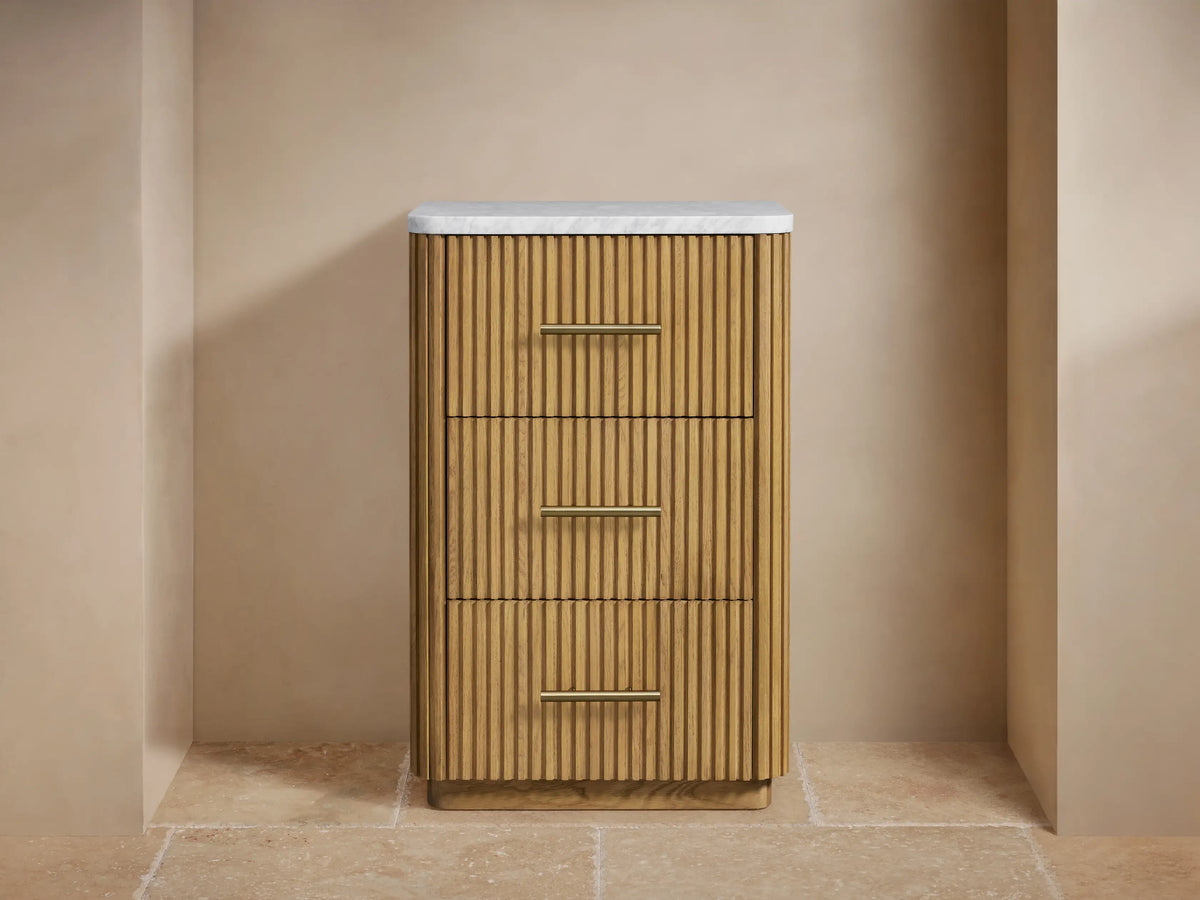 Finnley Short Etagere showcasing a partially opened oak wood drawer with vertical grooves, holding folded white towels and polished metal handles.