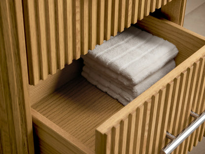 Finnley Short Etagere with vertical oak slats, three drawers with silver handles, and a white stone top, on a stone floor.