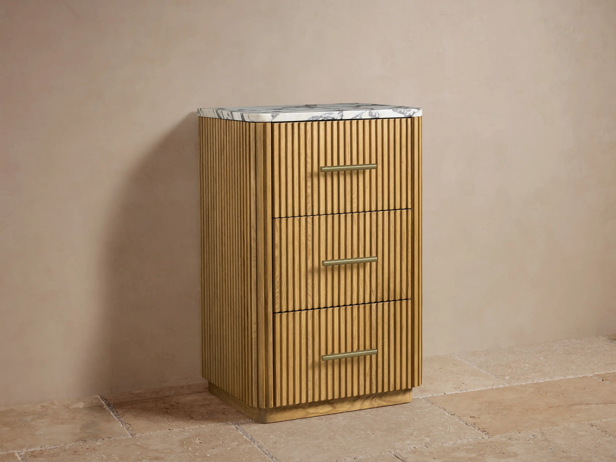 Finnley Short Bath Cabinet in light oak with reeded paneling, white marble top, 3 drawers with brass bar pulls. Styled with towels and decor.