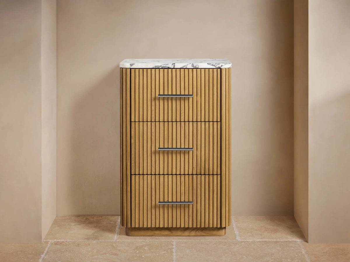 Finnley Short Bath Cabinet: light oak with vertical slats, white marble top, 3 drawers with silver pulls, against a beige wall.