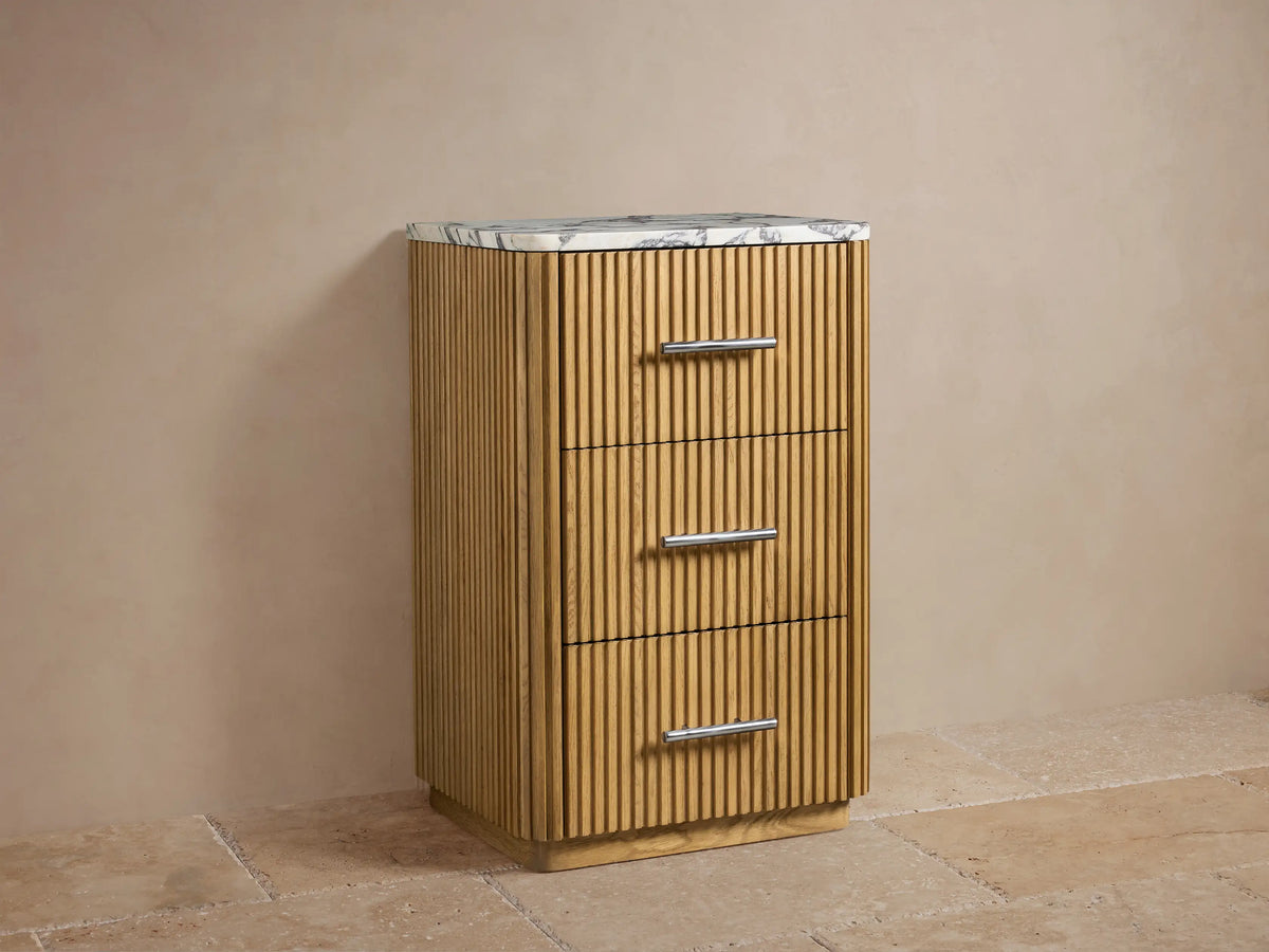 Close-up of Finnley Short Bath Cabinet's open oak drawer with fluted front, polished nickel handle, and two folded beige towels inside.
