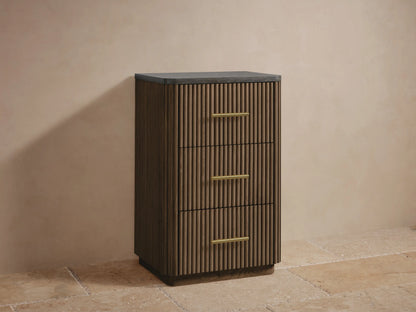 Finnley Short Bath Cabinet with dark, textured stone top, reeded oak wood, and a horizontal brass handle. Close-up, angled.