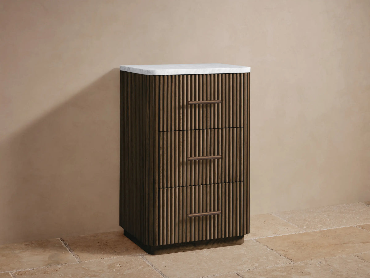 Open drawer of Finnley Short Bath Cabinet in warm oak with vertical fluting, holding folded white towels. Bronze handle on right.