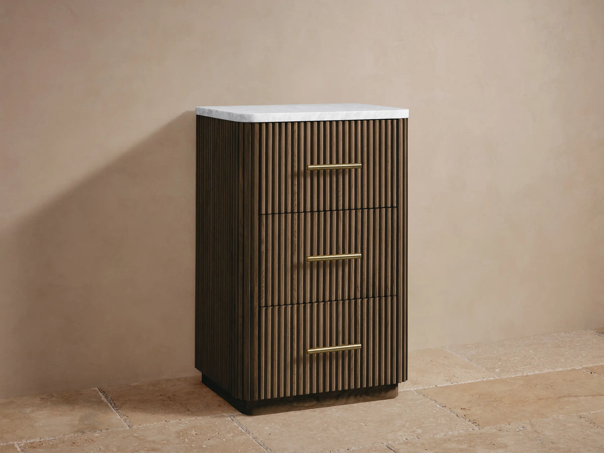 Close-up of Finnley Short Bath Cabinet top. White honed marble, rounded edge, dark fluted wood, polished brass handle.