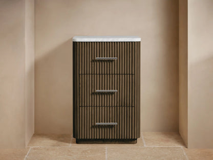 Finnley Short Bath Cabinet: dark fluted wood, 3 drawers with silver pulls, white marble top, towels & flowers on top.