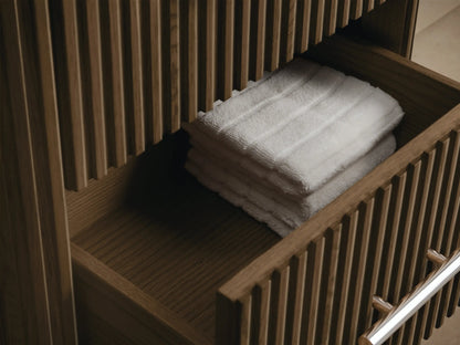 Close-up of Finnley Short Bath Cabinet. White Carrara marble top, dark fluted oak wood, polished nickel handle.