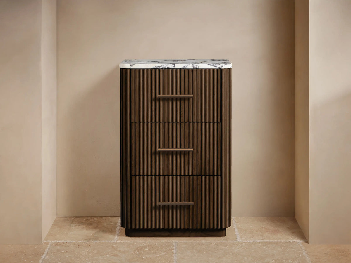 Finnley Short Bath Cabinet, dark brown fluted wood, white marble top, 3 drawers with bronze handles. Towels & decor on top.
