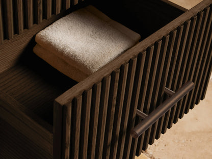 Angled close-up of Finnley Short Bath Cabinet: white marble top with dark veins, dark fluted wood, bronze handle.