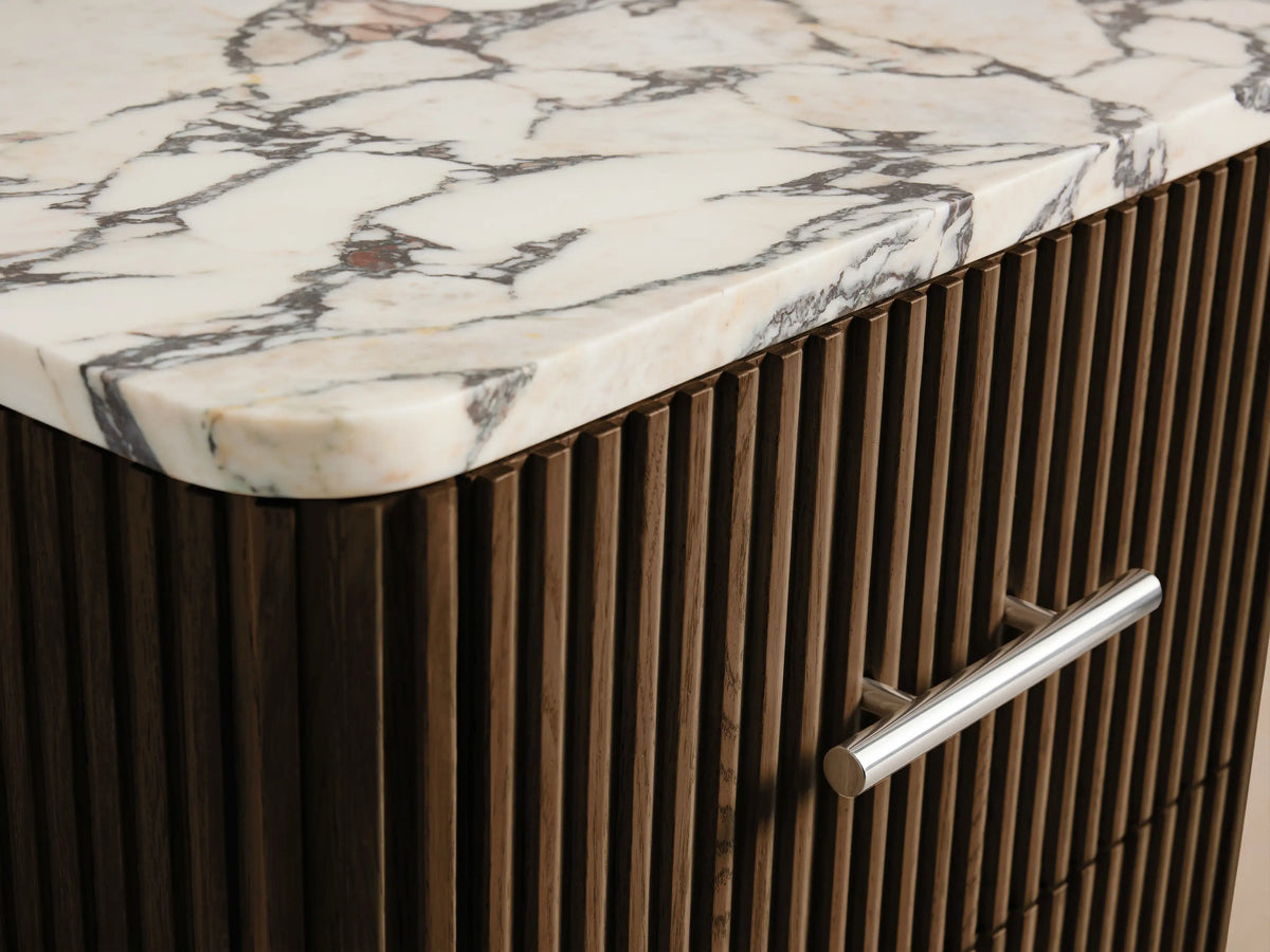 Finnley Short Bath Cabinet: Dark brown ribbed wood, 3 drawers with polished nickel handles, white veined marble top, on tiled floor.