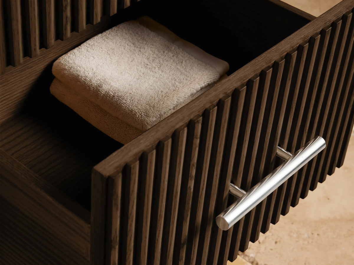 Close-up of Finnley Short Bath Cabinet, white marble top with dark veins, dark brown fluted wood, polished nickel handle.
