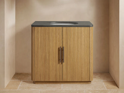 Finnley Single Vanity with light oak fluted cabinet, dark stone top, white oval sink, bronze faucet, and handles.