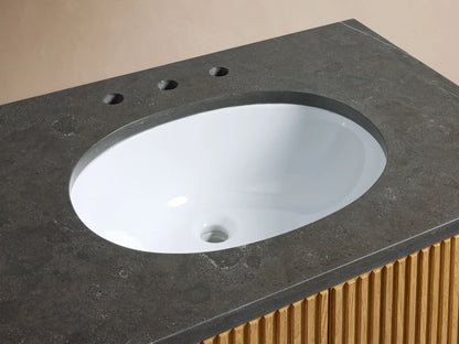 Oval ceramic undermount sink set in a dark stone top with polished nickel faucet handles and soap on the right.