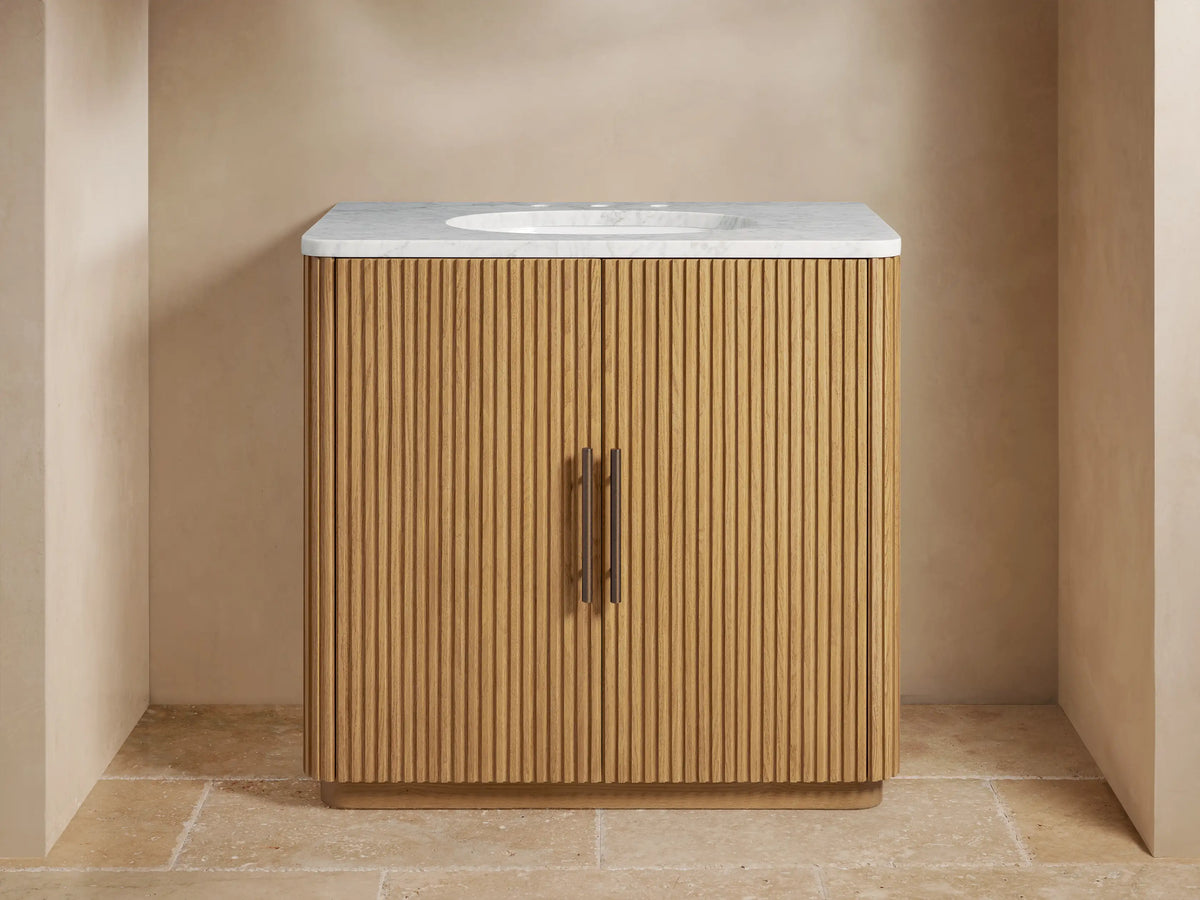 Finnley Single Vanity with light oak reeded wood cabinet, white marble top, oval sink, bronze faucet, and pulls.