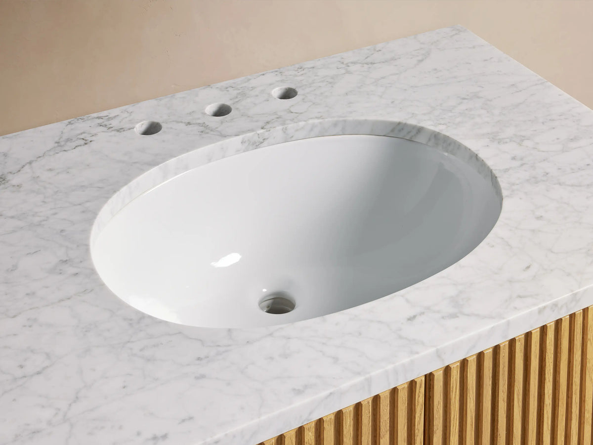 Close-up of Finnley Single Vanity with white oval sink, white Carrara marble top, bronze faucet, and light wood slatted base.