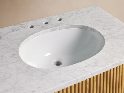 Oval ceramic sink set in Carrara marble top, surrounded by brass hardware and accessories, atop Finnley Single Vanity.