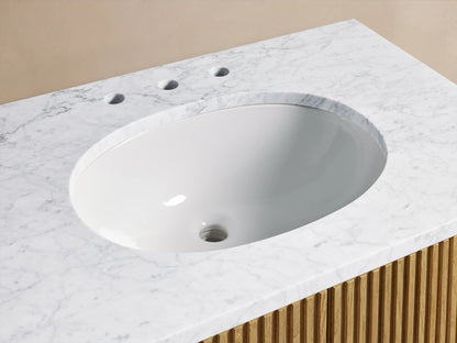 Oval ceramic sink set in Carrara marble top, featuring brushed nickel faucet and handles. Oak wood vanity with towel nearby.
