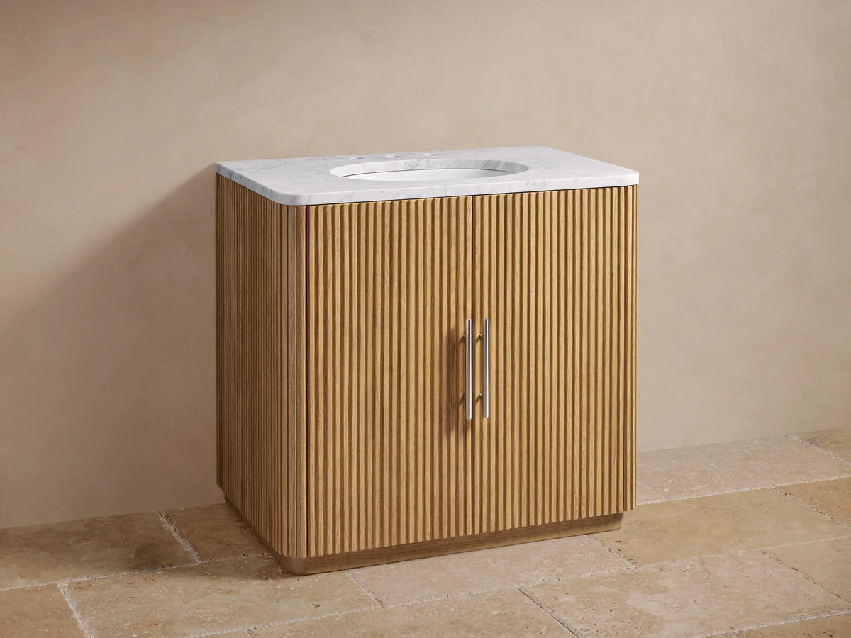 Finnley Single Vanity with oak wood slatted front, Carrara marble top. Two polished nickel door handles, oval ceramic sink.