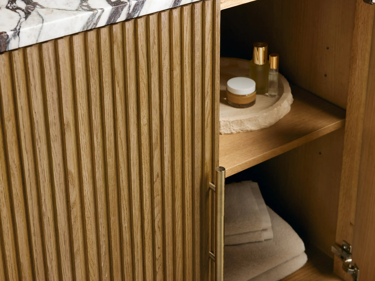 Finnley Single Vanity with white oval sink, white and brown marble top, brushed gold faucet, and stone soap dispenser.