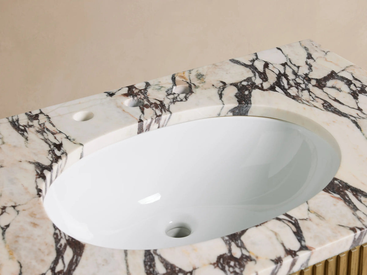 Finnley Single Vanity: White oval sink in Calacatta Viola marble top with dramatic dark veins, chrome faucet, small towel, decor.