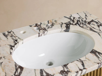 Finnley Single Vanity: White oval sink in Calacatta Viola marble top with dramatic dark veins, chrome faucet, small towel, decor.