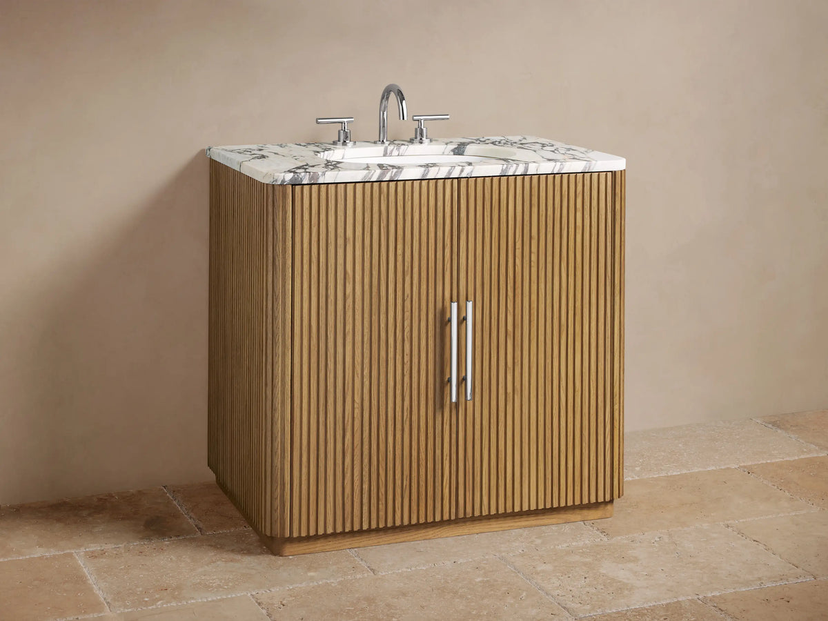 Close-up of Finnley Single Vanity's fluted oak door, partially open, showing toiletries & white towels inside. Veined marble top.