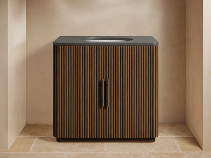 Finnley Single Vanity: dark wood fluted cabinet, bluestone top, white oval sink, bronze faucet, in a modern beige bathroom.