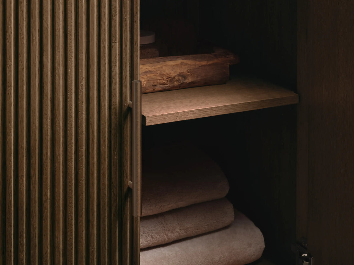Finnley Single Vanity. White oval undermount sink set in dark textured stone countertop with 3 faucet holes. Part of oak slatted cabinet visible.