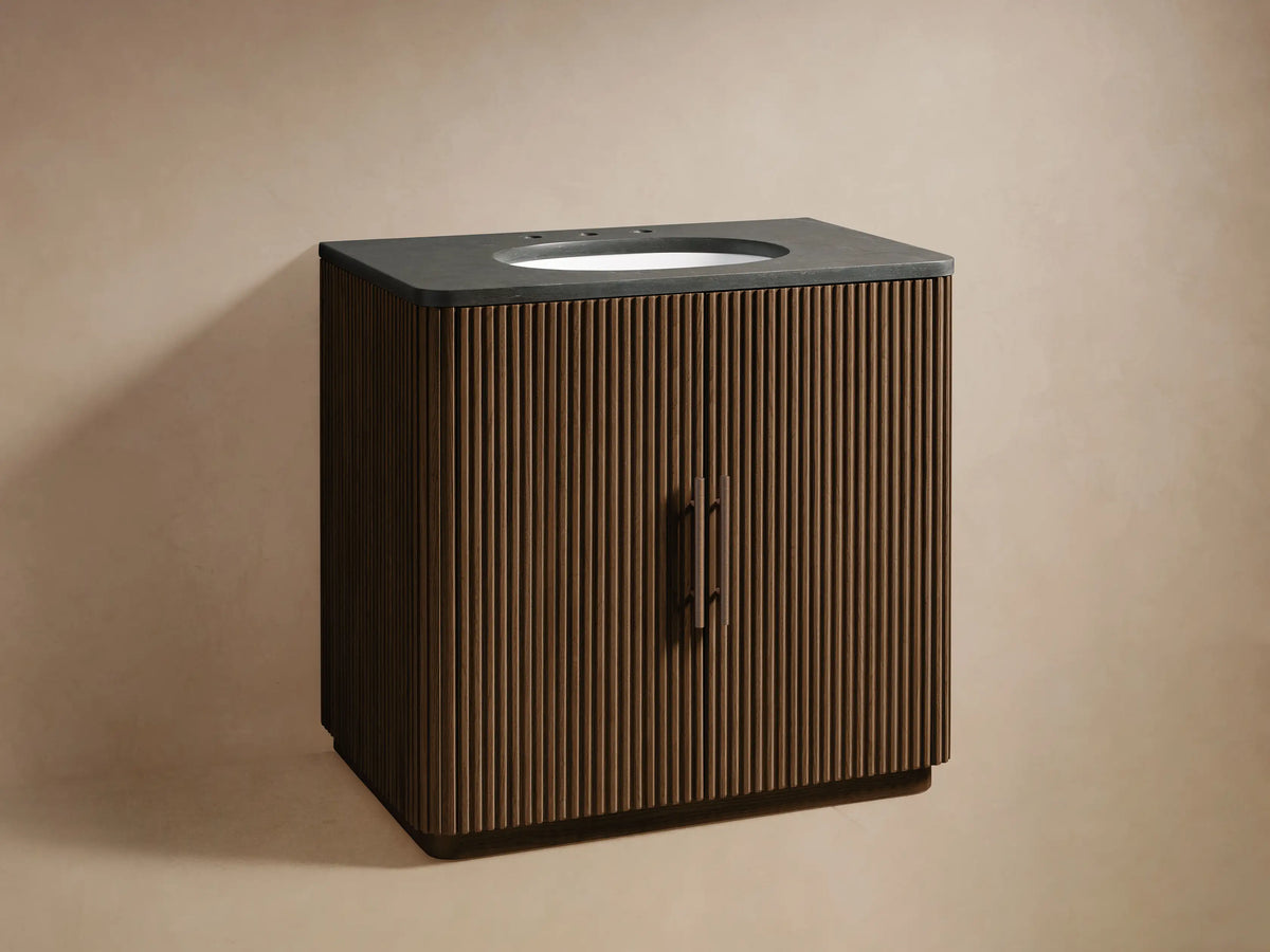 Finnley Single Vanity: Dark slatted wood cabinet with a dark stone top, white oval sink, and bronze faucet, angled on a beige background.