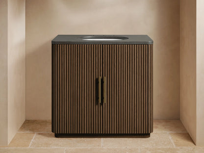 Finnley Single Vanity with dark reeded wood cabinet, bluestone top, white sink, brass faucet and handles, in a bathroom.