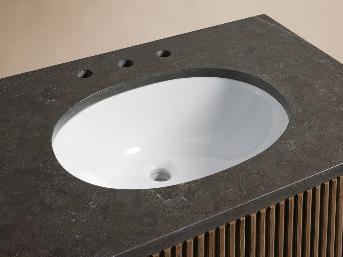 Angled close-up of Finnley Single Vanity with a white oval sink, dark gray stone top, brass faucet, and slatted wood cabinet.