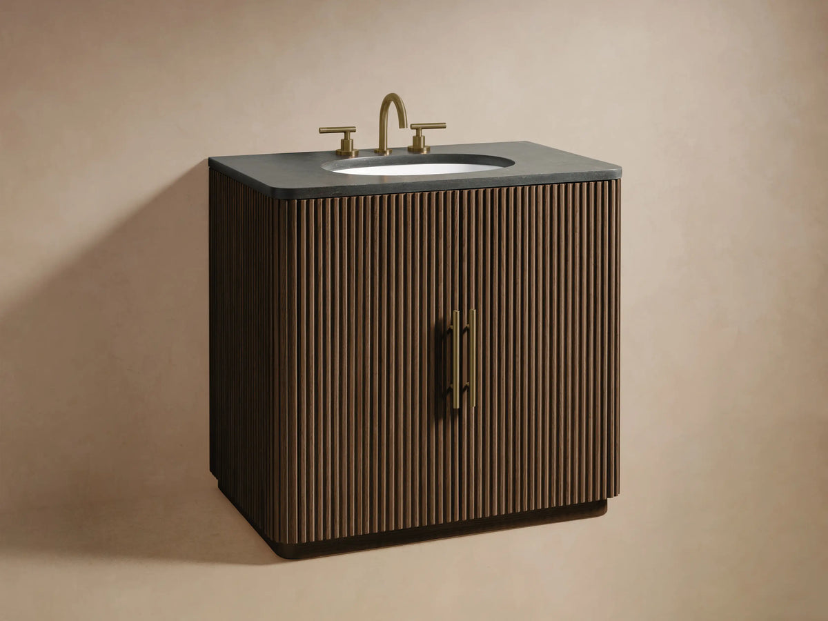 Close-up of the Finnley Single Vanity: dark brown reeded door with a brass handle, partially open, revealing wood shelves with towels and a wooden tray.