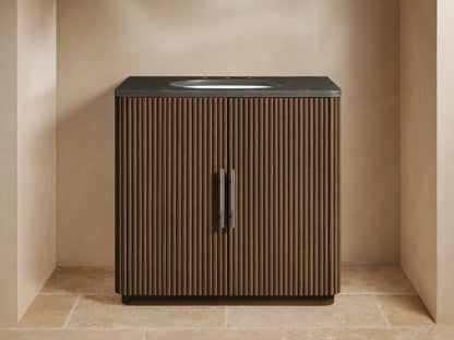 Finnley Single Vanity with dark fluted wood cabinet, dark stone top, white oval sink, chrome faucet, set in a beige room.