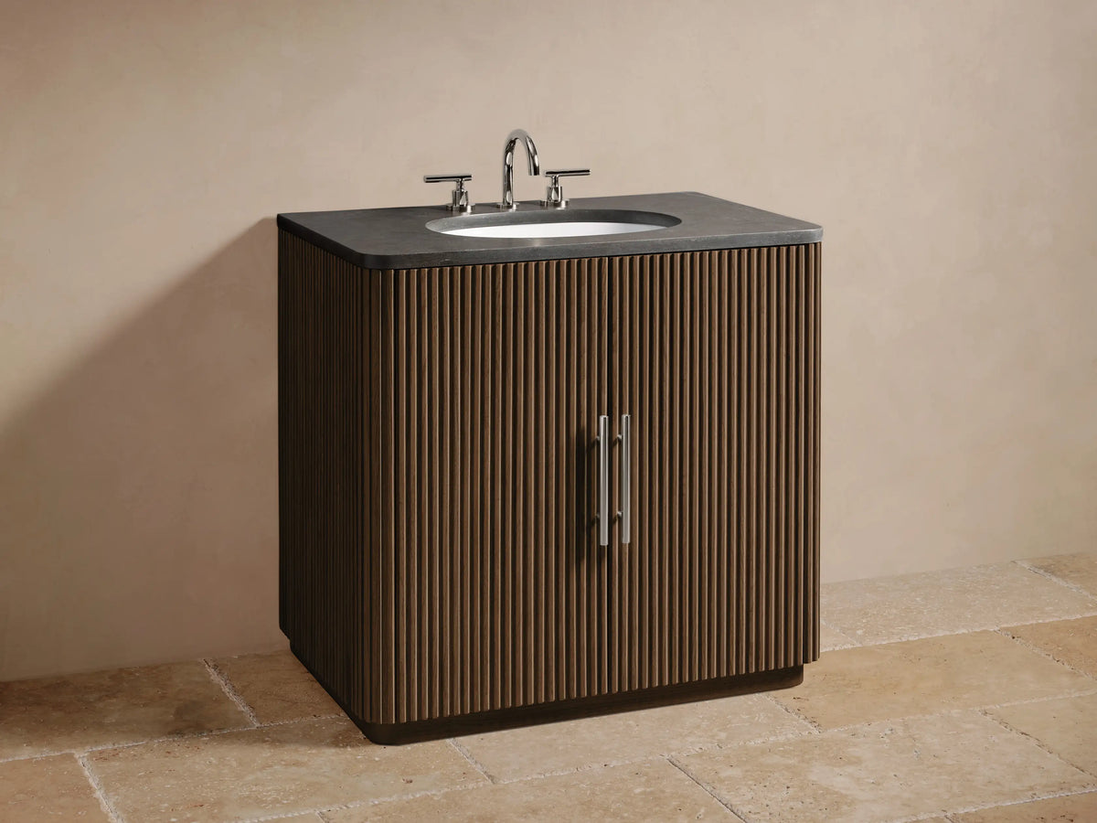 Close-up of Finnley Single Vanity's open, fluted oak cabinet door with polished nickel handle, revealing shelf and towels inside.