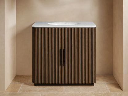 Finnley Single Vanity with dark fluted wood cabinet, white marble top, integrated sink, and bronze faucet & handles in a bathroom.