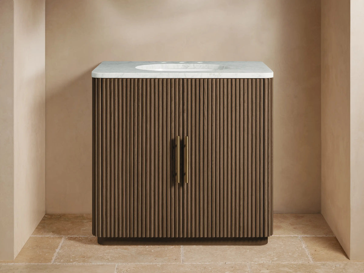 Finnley Single Vanity with dark fluted wood cabinet, white marble top, brass faucet & hardware in a neutral bathroom.