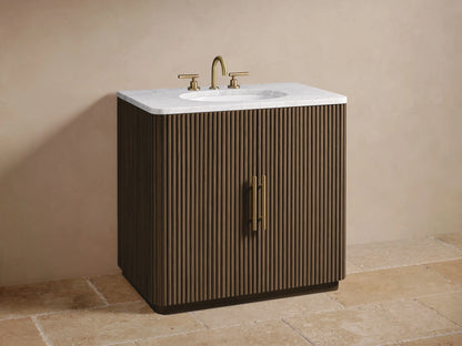 Finnley Single Vanity's open fluted dark oak door with gold handle. Inside: light wood shelf with rustic bowl and stacked beige towels.