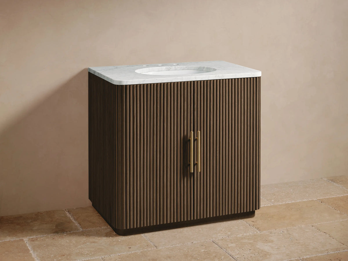 Finnley Single Vanity: Dark brown fluted wood cabinet, white marble top, oval sink, brass widespread faucet & handles.