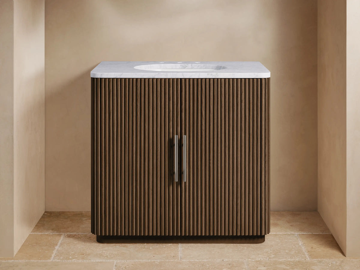 Finnley Single Vanity: Dark fluted wood cabinet with white marble top, chrome faucet, and undermount sink, centered in a bathroom.
