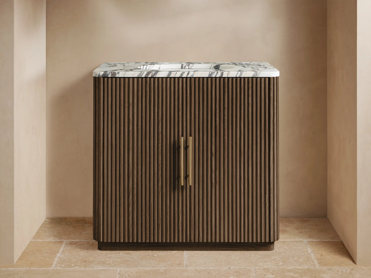 Finnley Single Vanity with dark brown fluted wood cabinet, white marble top, gold faucet, and two gold handles.