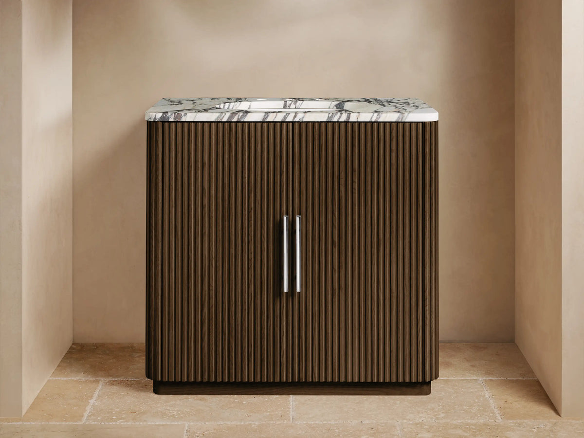Finnley Single Vanity: fluted dark oak wood cabinet, white Carrara marble top, silver faucet, & pulls in a neutral setting.