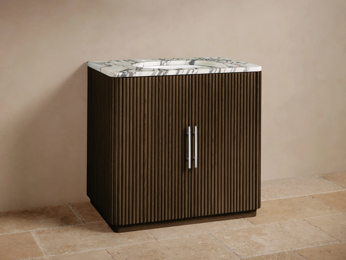 Finnley Single Vanity: Dark brown fluted wood cabinet with white Carrara marble top, chrome faucet, and handles, on a tiled floor.