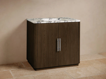 Finnley Single Vanity: Dark brown fluted wood cabinet with white Carrara marble top, chrome faucet, and handles, on a tiled floor.