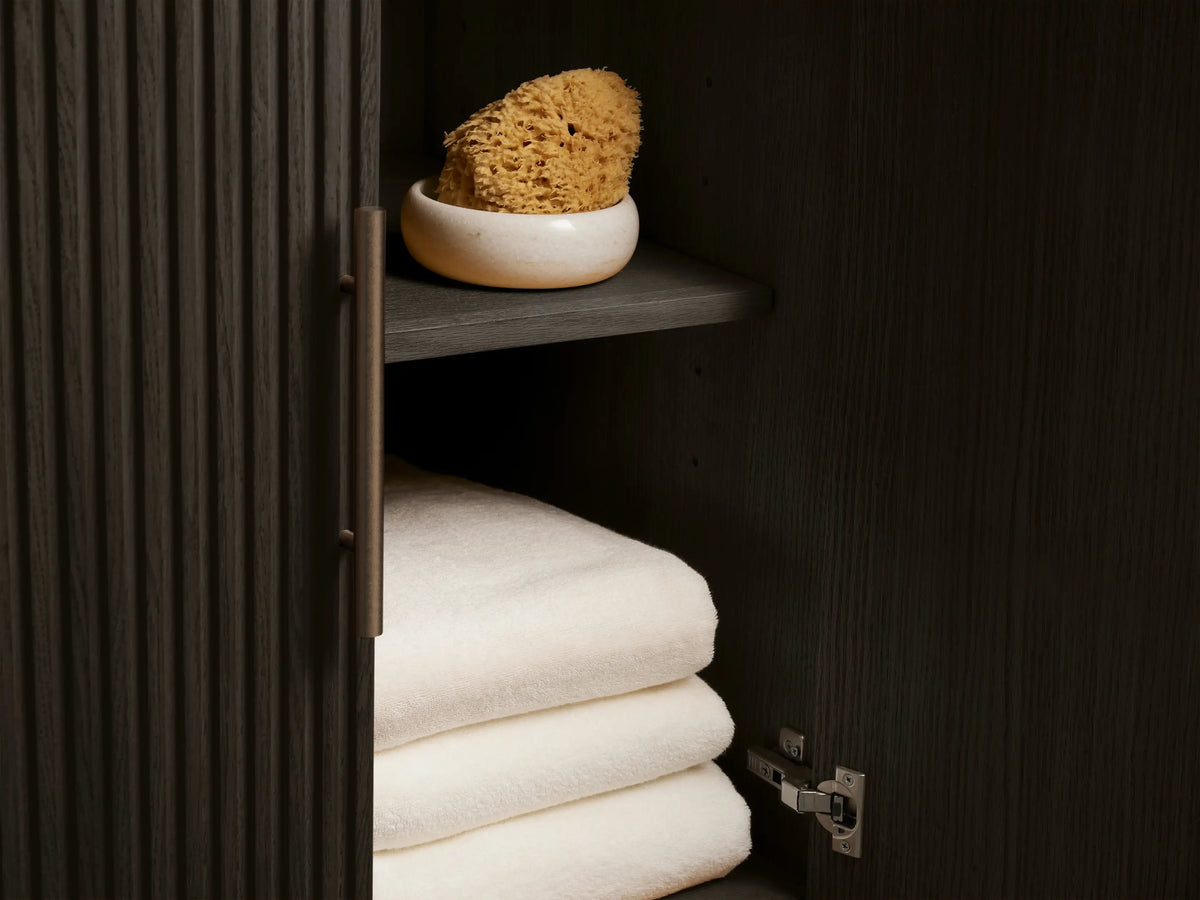 Finnley Wide Single Vanity close-up: dark bluestone top, oval white sink, bronze faucet, white towel, & marble soap dish.