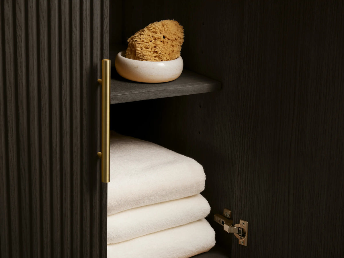 Close-up of Finnley Wide Single Vanity with dark bluestone countertop, white oval sink, brass widespread faucet, white towel, fluted cabinet.